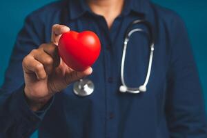 Hand of a doctor holding a red heart shape while standing on a blue background photo