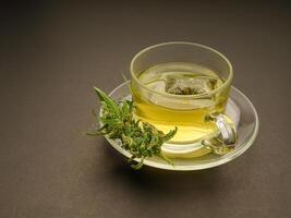 Cannabis tea in a teacup and marijuana buds flower on a gray background photo