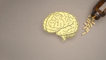 Brain shape made from paper and pills capsules with a bottle on a gray background photo