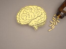 Brain shape made from paper and pills capsules with a bottle on a gray background photo