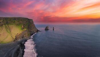Dramatic aerial view of a rugged cliff and black sand beach in Iceland at sunset. Vibrant sky colors and distant sea stacks create a breathtaking coastal scene. photo