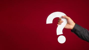 Hand of a man in a black shirt holding a white question mark while standing with a red background photo