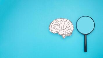A brain shape made from paper and a magnifying glass on a blue background photo