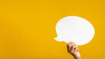 A speech bubble concept. Hand holding of an empty white speech balloon on yellow background with copy space for text photo