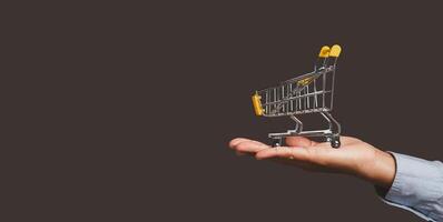 An empty yellow mini shopping trolley on the palm people while standing on gray background. photo