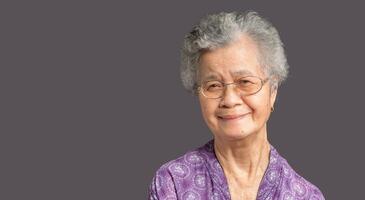 An elderly Asian woman looking at the camera with a smile while standing against on gray background photo