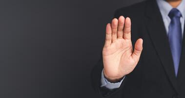 Businessman making stop gesture with his hands while standing on gray background. photo