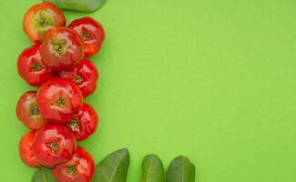 Ripe red acerola cherries and green leaves isolated on a light green background. photo