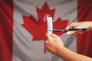End of COVID-19 or Coronavirus. Close-up of a medical mask in a fist over on Canada flag background. End of quarantine back to Normal life photo