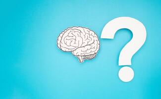 Brain shape made from paper and a white question mark against a blue background photo