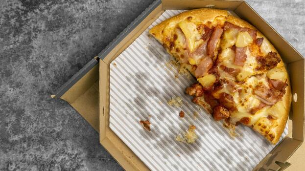 Top view half of pizza topped bacon, pineapple, and cheese in a takeaway cardboard box, delivery foods package on the grey concrete table. photo