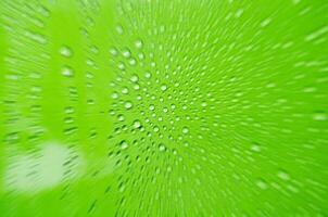 Zooming into rain water droplets on green glass background. Close up of rain drop from below photo