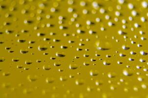 Side view of raindrops forming patterns on a smooth surface on yellow background. Fresh rain texture photo