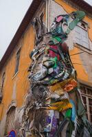 A three-dimensional rabbit's head made from recycled materials adorns a yellow building in Porto, Portugal. The aged structure adds to the urban charm. photo