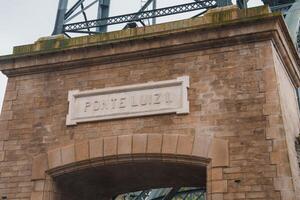 Detailed view of the stone archway and steel elements of Ponte Luiz I in Porto, Portugal. The light brown stone bricks and white plaque highlight its architectural significance. photo