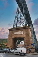 The iconic Ponte Luiz I bridge in Porto, Portugal, features a double-deck iron structure and a massive stone archway. Vehicles and pedestrians add to the bustling scene. photo