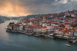 Colorful buildings with red-tiled roofs cascade down to the Douro River in Porto, Portugal. The Dom Luis I Bridge spans the river, connecting to Vila Nova de Gaia. photo