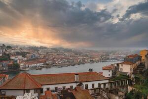 Stunning view of Porto, Portugal at sunset with the Douro River dividing the city. Traditional red-tiled roofs and a mix of historic and modern architecture are visible. photo