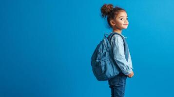 Portrait of cute african american girl with backpack standing on blue background photo