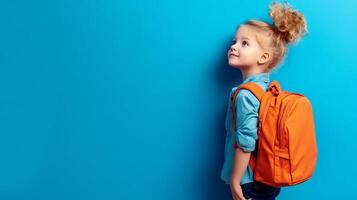 A little girl with a backpack standing against a blue wall photo