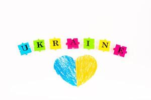 puzzles of letters Ukraine on a white background and paper heart, painted in the color of the flag of Ukraine photo
