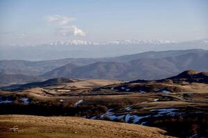 A landscape of rolling green meadows with snow-capped mountain peaks in the background. High quality photo