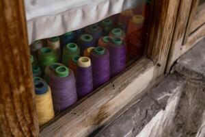 Colorful spools of thread neatly arranged in a wooden window, evoking the charm of craftsmanship and handmade work. High quality photo
