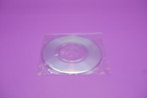 A compact disc isolated on a purple background. A compact disc wrapped in clear plastic. photo