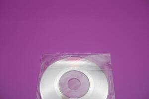 A compact disc isolated on a purple background. A compact disc wrapped in clear plastic. photo