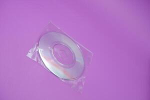 A compact disc isolated on a purple background. A compact disc wrapped in clear plastic. photo