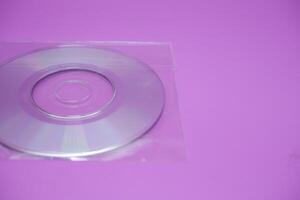 A compact disc isolated on a purple background. A compact disc wrapped in clear plastic. photo