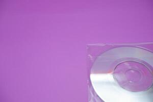 A compact disc isolated on a purple background. A compact disc wrapped in clear plastic. photo