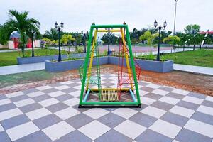 hanging swing chair that is usually found in parks or playgrounds. hanging swing chair made of iron with a combination of yellow, green, and red colors. photo