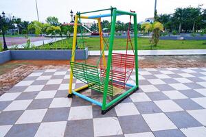 hanging swing chair that is usually found in parks or playgrounds. hanging swing chair made of iron with a combination of yellow, green, and red colors. photo