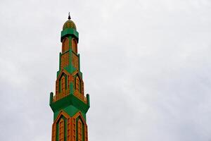 mosque tower with a combination of green and yellow. Mosque minaret against a cloudy sky background photo