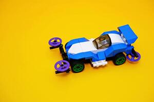 blue racing car assembled from plastic blocks. toy car isolated on yellow background photo