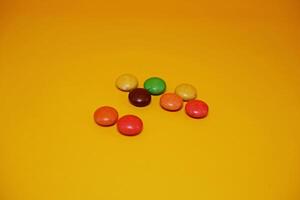 chocolate balls coated with colorful candy. colorful chocolate candy isolated on yellow background. photo