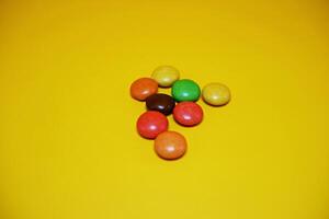 chocolate balls coated with colorful candy. colorful chocolate candy isolated on yellow background. photo