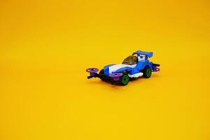 blue racing car assembled from plastic blocks. toy car isolated on yellow background photo