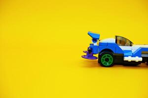 blue racing car assembled from plastic blocks. toy car isolated on yellow background photo