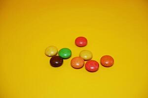 chocolate balls coated with colorful candy. colorful chocolate candy isolated on yellow background. photo