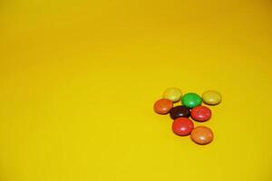 chocolate balls coated with colorful candy. colorful chocolate candy isolated on yellow background. photo