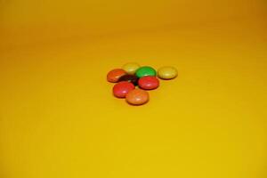 chocolate balls coated with colorful candy. colorful chocolate candy isolated on yellow background. photo