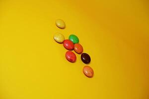 chocolate balls coated with colorful candy. colorful chocolate candy isolated on yellow background. photo