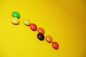 chocolate balls coated with colorful candy. colorful chocolate candy isolated on yellow background. photo