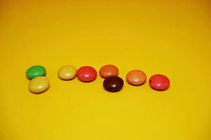 chocolate balls coated with colorful candy. colorful chocolate candy isolated on yellow background. photo