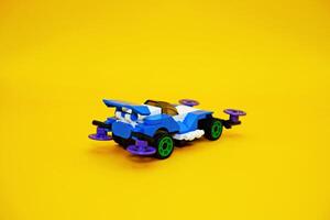 blue racing car assembled from plastic blocks. toy car isolated on yellow background photo