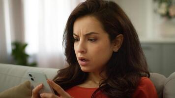 Shocked mad displeased Caucasian woman stressed nervous female girl use mobile phone chatting app texting online receiving bad message SMS smartphone error connection problem losing game at home sofa photo
