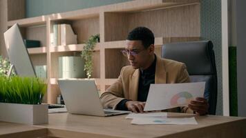 African American man entrepreneur office manager guy male businessman working at desk with laptop read documents check graphics charts business paperwork analyzing data upset financial problem mistake photo