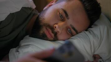 Caucasian man lying in bed bedroom user mobile phone smartphone cellphone gadget technology male guy connected scrolling website browsing network cyber ecommerce chatting internet distance communicate photo